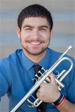 brass coach Connor Bagheri smiles while holding his trumpet in front of him.